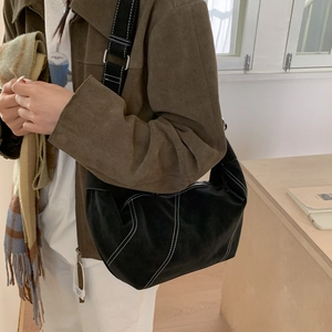 Détail du sac bandoulière en daim noir avec surpiqûres blanches et large bandoulière