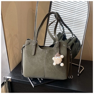 Detail of olive green suede tote bag featuring drawstring closure and furry monster charm