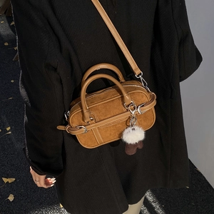 Detailed close-up of a caramel brown boston bag with plush charm and white contrast stitching