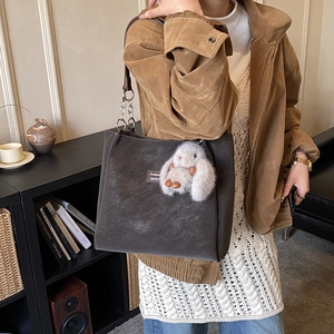 Detail of dark tote bag with metal chain strap and plush bird charm in warm room
