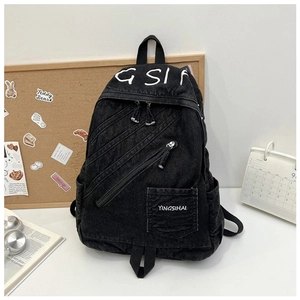 Macro detail of black denim backpack with diagonal zipper design and hand-drawn letters