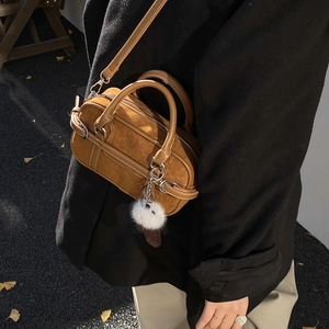 Brown suede Boston bag styled on a black wool coat with autumn street background