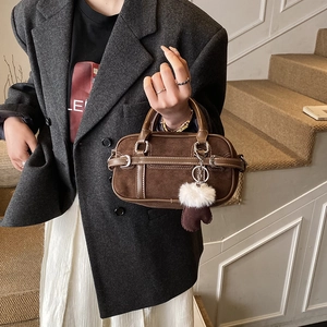 Detail of a brown suede Boston bag featuring a leather strap with decorative metal buckle