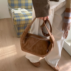 Détail d'un sac bandoulière en daim marron avec surpiqûres blanches et anse nouée