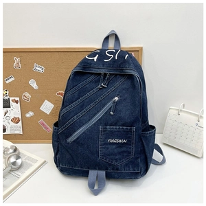 Detail of dark blue denim backpack with multi-zipper pockets on a white desk