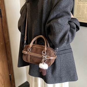 Brown suede Boston bag with fuzzy ball and glove charms worn by a model