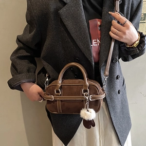 Close-up of brown frosted leather Boston bag featuring soft pom-pom and metal accents