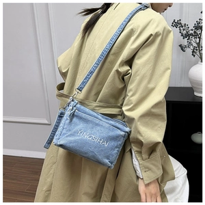 Side view of denim crossbody bag with white embroidery and metallic strap buckles