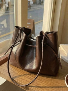 Dark brown oil wax leather tote bag with knotted strap detail on a sunlit wooden table
