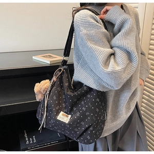 Detail of black floral corduroy tote bag with plush bear charm and white woven label