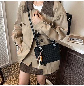 Detail of woven texture black tote bag with wooden bead charm on a khaki coat model