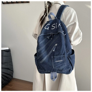 Detail of dark blue denim backpack featuring embroidered GSI logo and side zipper pockets