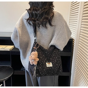 Détail d'un grand sac cabas noir à motifs de cœurs avec un porte-clé ours en peluche