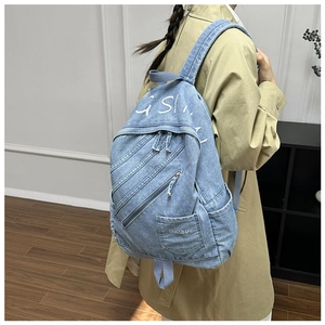 Detail of light blue denim backpack showing multi-layer zippers and GSL letter print