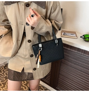 Detail of black checkerboard handbag featuring vintage wooden bead charm and silver hardware