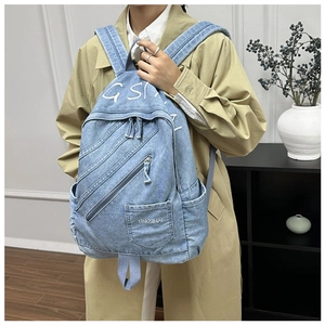 Detail view of light blue denim backpack with metal zippers on a trench coat model