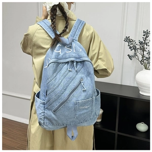 Close-up of light blue denim backpack with multi-zipper pockets and white letter print