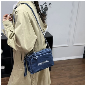 Detailed shot of a blue denim crossbody bag with white YINGSIHAI embroidery and zipper pockets