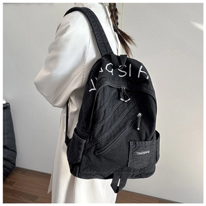 Detail of black denim backpack with white embroidery and multiple zippered pockets on model