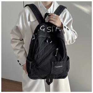 Model showing a large black denim backpack with GSIA embroidery and multiple zipper pockets