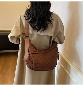 Brown quilted crossbody hobo bag with wide shoulder strap shown on a model