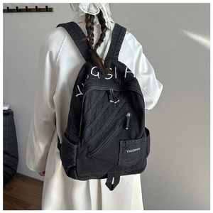 Detail of vintage black denim backpack with white embroidery and diagonal zippers
