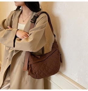 Detail of a brown quilted half-moon bag featuring diamond patterns and wide shoulder strap