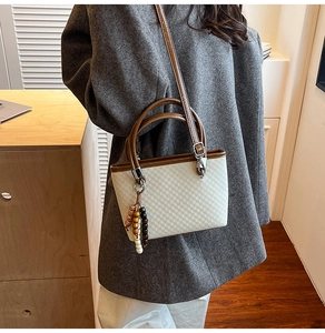 Detail of a minimalist checkered bucket bag featuring brown leather straps and wooden beads