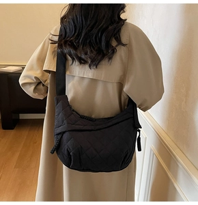 Detail view of black quilted crossbody bag with woven zipper pull on a model