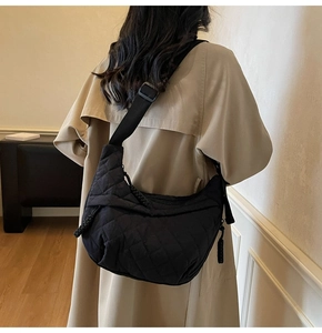Model wearing a large black quilted crossbody crescent bag with a beige trench coat