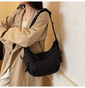 Detail of black quilted crossbody bag with adjustable strap worn on khaki coat