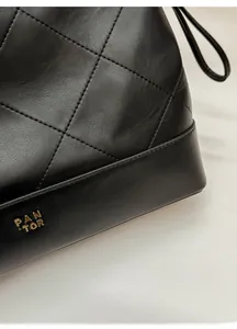 Close-up of black quilted leather bag with gold PANTOR metal logo and premium stitching