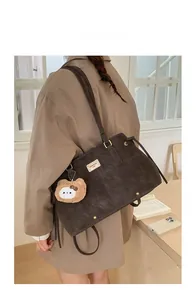 Detail of dark brown tote bag with metal nameplate and cute brown plush bear charm