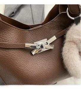 Close-up of pebble grain brown leather bag with silver twist lock and plush charm