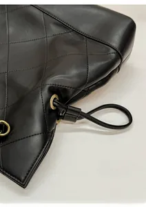 Detailed close-up of drawstring closure on black quilted leather tote with gold eyelets