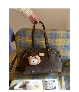 Detail of dark brown tote bag with metal logo and cute plush bear on a cozy chair