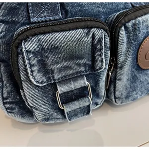 Macro detail of dark blue denim bag showing zipper pocket, metal buckle, and fabric texture