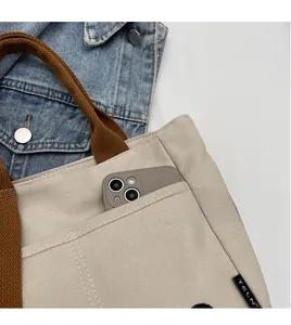 Détail du sac fourre-tout en toile beige montrant l'étiquette et la grande poche externe
