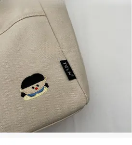 Détail d'un sac cabas en toile beige avec broderie cartoon et étiquette tissée latérale