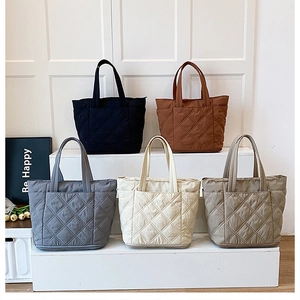 Detail view of large quilted tote bags in five colors on a minimalist display stand