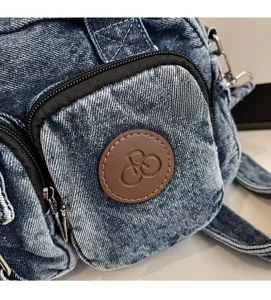 Detail of blue denim shoulder bag showing washed texture and brown leather logo patch