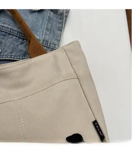 Détail du sac cabas en toile beige montrant l'étiquette latérale et la sangle en coton brun