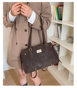 Close-up of a dark brown matte tote bag with gold hardware and side drawstring details