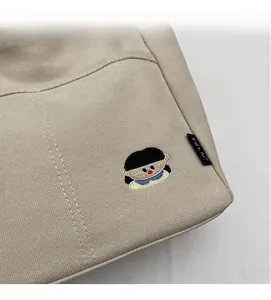 Détail du sac cabas en toile beige avec broderie portrait et étiquette tissée noire