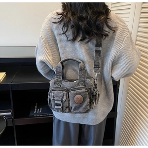 Detailed view of gray washed denim crossbody bag featuring double front pockets and round logo