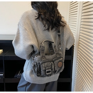 Detail of vintage denim crossbody bag showing washed black texture and front zip pockets