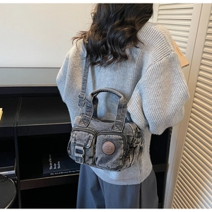 Detail of dark grey washed denim crossbody bag featuring dual front pockets and logo patch