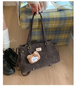 Detail of dark brown matte tote bag with teddy charm and brand logo on wooden floor