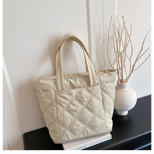 Close-up of beige quilted tote bag with diamond pattern on black table in home setting