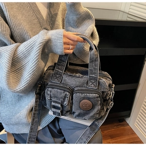 Detail of vintage gray denim bag showing large zip pockets and a brown leather logo patch